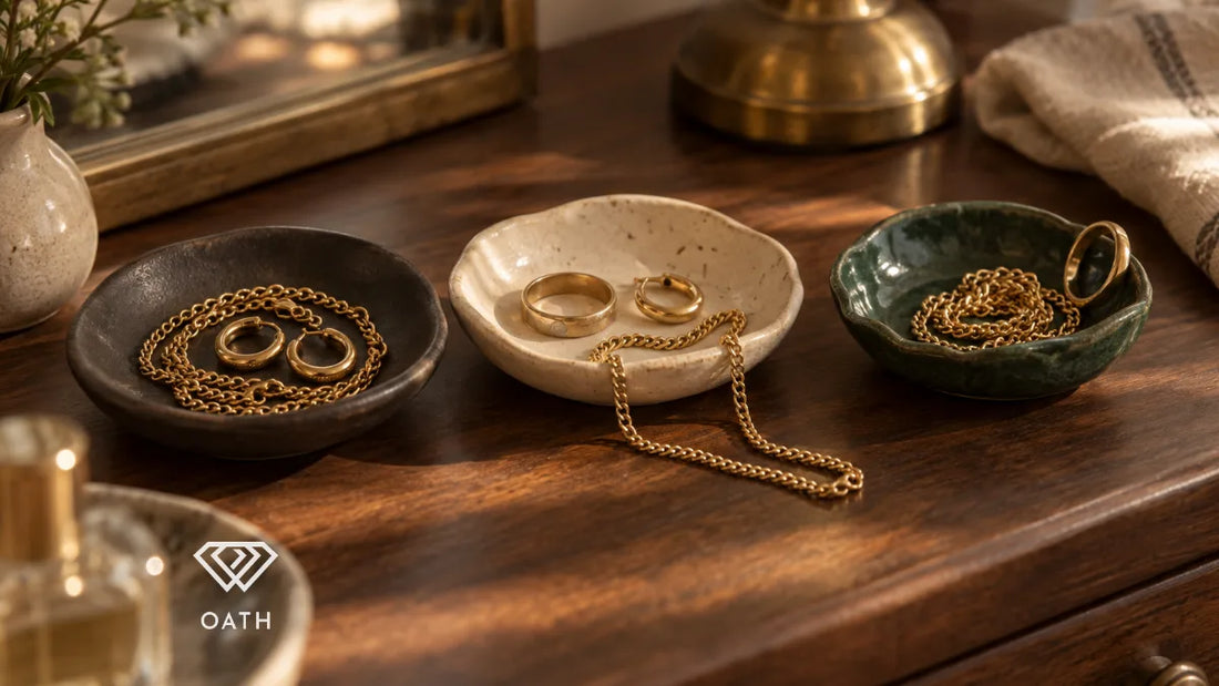 Gold chains, hoop earrings and rings in three small ceramic dishes on a walnut dresser