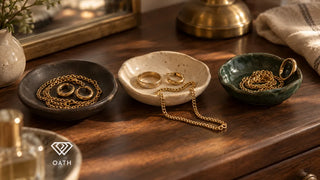 Gold chains, hoop earrings and rings in three small ceramic dishes on a walnut dresser